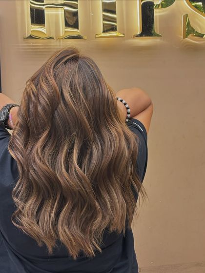 This back view showcases a beautiful, warm-toned hair color styled into beachy waves. The color is rich and dimensional, giving the hair a healthy, vibrant look.