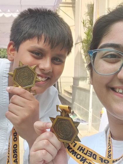 Two young students proudly showing their star-shaped medals from the Delhi State Championship.