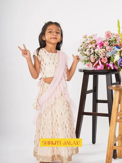 Peace, love, and great style. This little girl is posing in a cream and gold printed lehenga with a soft pink ruffled dupatta.