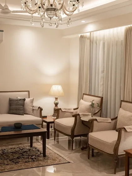 This living room setup is a study in comfy, classic design. We paired neutral-toned sofas and armchairs with dark wood tables and a traditional rug, all under the warm glow of a crystal chandelier, to create a timeless and welcoming space.