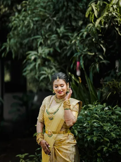 The bride surrounded by greenery, her golden saree and jewelry glowing in the natural light.