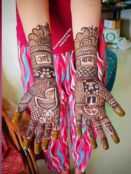 A full view of the "Mom To Be" and "Dad To Be" henna design, showcasing the intricate patterns on the forearms.