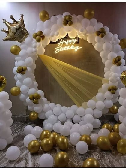 A royal-themed birthday decoration in white and gold. The balloon ring is accented with a golden crown foil balloon and a 'Happy Birthday' neon sign for a truly regal feel.