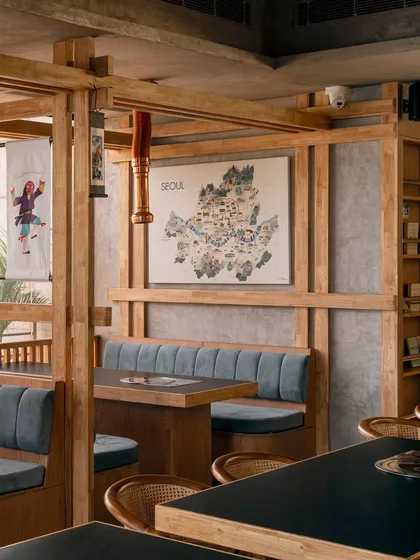 A framed map of Seoul hangs as a central art piece, reinforcing the restaurant's identity. The combination of soft blue upholstery, warm wood, and curated decor makes this booth area feel both cozy and culturally rich.