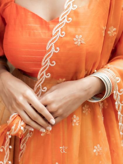 A close-up of the embroidered orange organza dupatta, showcasing the fine craftsmanship and delicate floral motifs.