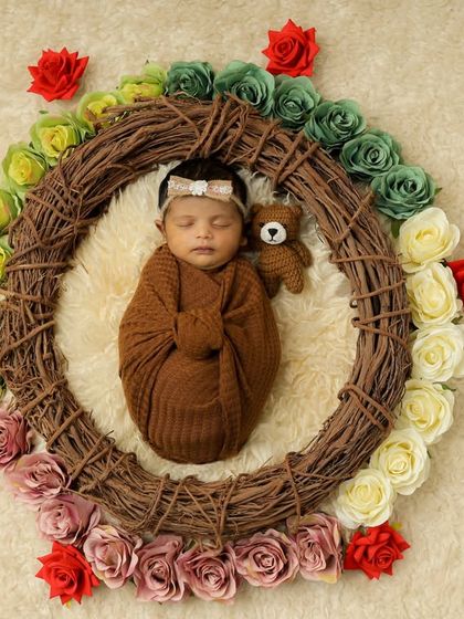 A newborn sleeps with a tiny teddy bear, encircled by a rustic wreath decorated with a gradient of colorful roses. This overhead shot is a beautiful composition of textures and colors.