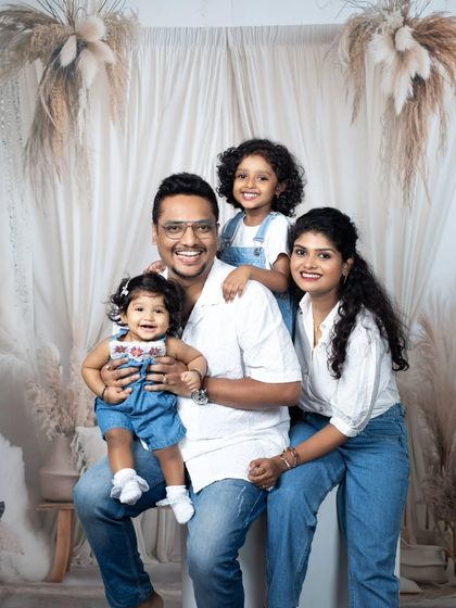 A happy family of four posing together in the studio, dressed in matching white and denim outfits for a clean, classic look.