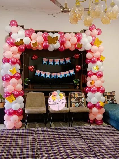 A pink and white butterfly-themed balloon arch set up in a living room.