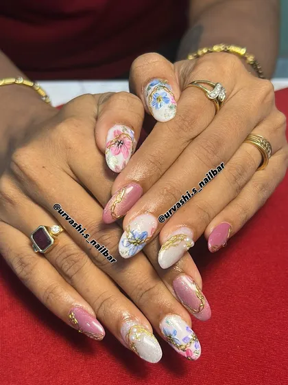 A royal garden on your fingertips. This design combines hand-painted pastel flowers with elegant gold chain details over a mix of mauve and pearly white nails.