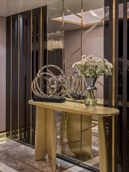 A custom console table with a unique, sculptural gold base, set against a wall of mirrored panels with brass inlays. This piece is designed to make a statement from the moment you enter a room.