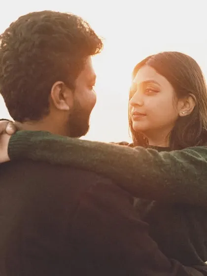 A beautiful over-the-shoulder shot where she embraces him, looking directly at the camera with a soft, loving expression. The golden light illuminates the scene, creating a warm and inviting portrait.