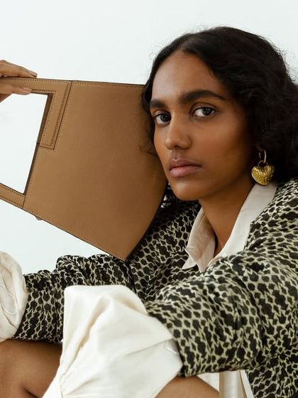 An editorial shot for Adisee handbags, where the model is crouched and holding the bag in a unique way. The styling is high-fashion and conceptual.