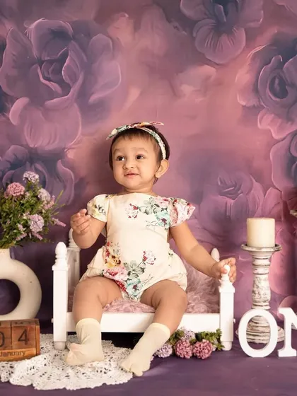 A regal portrait for a first birthday. The little one is seated on a miniature bed against a dreamy, lavender floral backdrop.