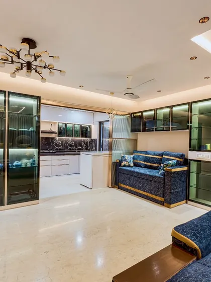 An open-plan living and dining area. The space features glass-fronted crockery units, a comfortable sofa, and a modern chandelier, all designed to create a sense of spaciousness and luxury.