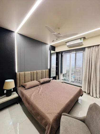 A modern bedroom designed for comfort and style. The room features a custom upholstered headboard, integrated side tables, and sophisticated wall paneling with ambient strip lighting to create a cozy and relaxing retreat.