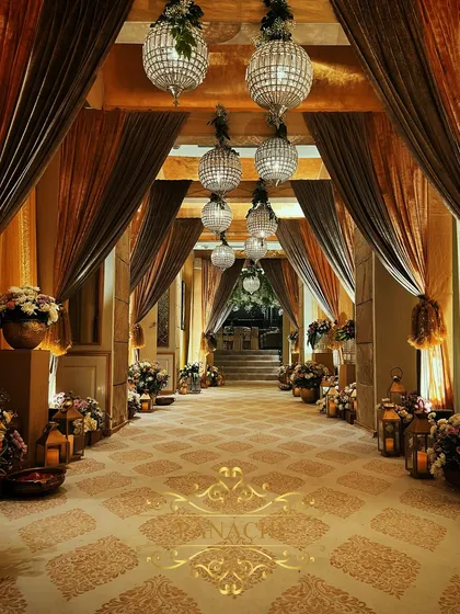 We create breathtaking entryways that transport you. This corridor at The Lodhi, Delhi, was transformed with layers of gold and brown drapes, floral arrangements, and spherical crystal chandeliers for a Roka ceremony.