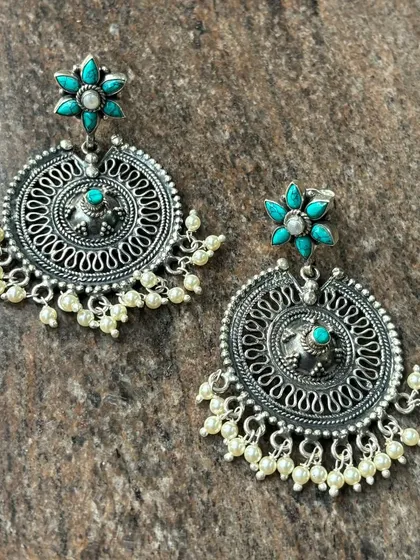 Another style of our oxidised silver chandbali earrings. This pair has a floral top with a turquoise stone and a circular drop with intricate filigree work.