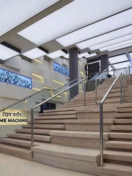 The grand staircase inside the museum, referred to as the 'Time Machine'. The design uses clean lines, modern materials like glass and steel, and dramatic back-lit panels to create a futuristic feel.