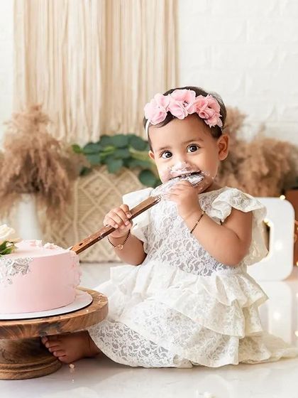 A sweet moment from a boho-themed cake smash, where the birthday girl is delicately tasting the frosting.