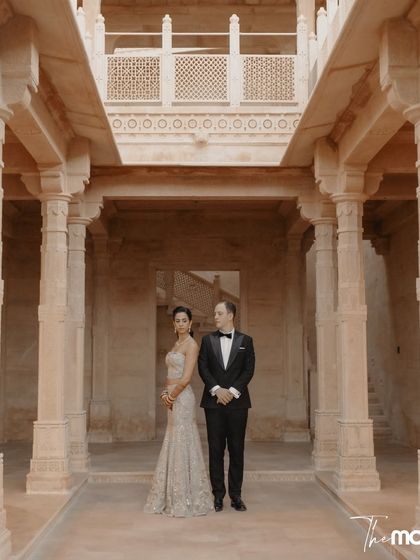 A formal portrait set within the majestic stone corridors of Suryagarh. The couple stands with a quiet confidence, their elegance perfectly matching the grandeur of their surroundings.