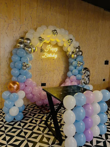 A pastel-themed 3rd birthday decoration with a balloon arch in light blue, pink, and white, accented with silver chrome balloons.