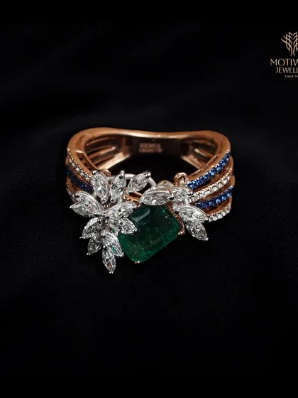 An artistic fusion of gemstones. This ring showcases a central emerald-cut green gem, flanked by clusters of marquise diamonds and accented with channels of blue sapphires.