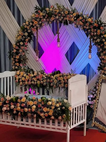 A close-up view of a white cradle lavishly decorated with peach and pink roses for a beautiful naming ceremony.