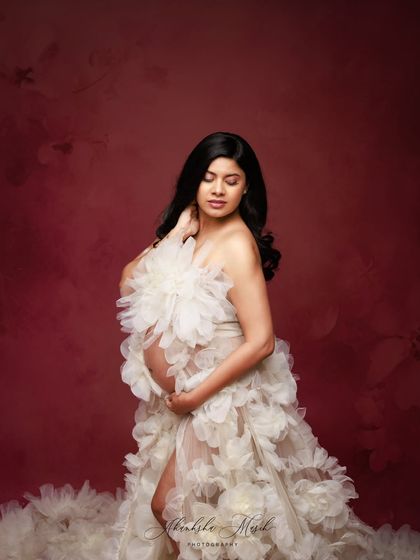 A quiet, introspective pose in the stunning white floral gown, highlighting its delicate texture and the mother's gentle connection with her bump.