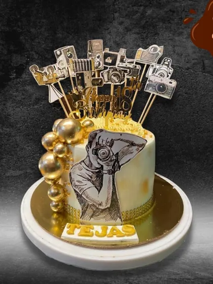 A perfect snapshot of a passion. This cake for a photographer is decorated with an illustration of a photographer and topped with an array of golden camera-themed toppers.