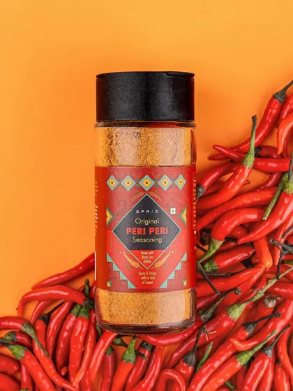 This image for a peri-peri seasoning uses a bed of vibrant red chillies and a bold orange background to make the product pop. This is a great example of a clean, product-focused shot that is ideal for e-commerce websites and online advertising.