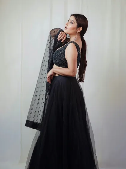 A graceful side-profile shot of the model in her black lehenga, holding the dupatta to create an elegant line.