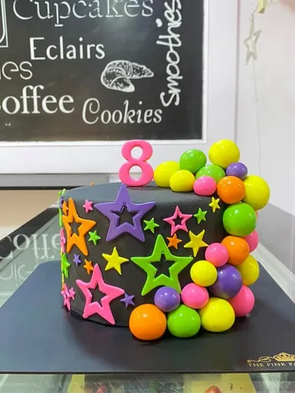 A vibrant neon-themed cake. The black base makes the colorful stars and spheres pop, creating a fun and energetic design for an 8th birthday party.