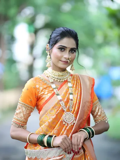 A full-length portrait of a bride in a stunning orange saree. The makeup is kept fresh and radiant to complement the bright color of her outfit.