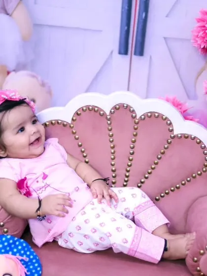 A relaxed and happy baby girl lounging on a pink couch during her photoshoot.