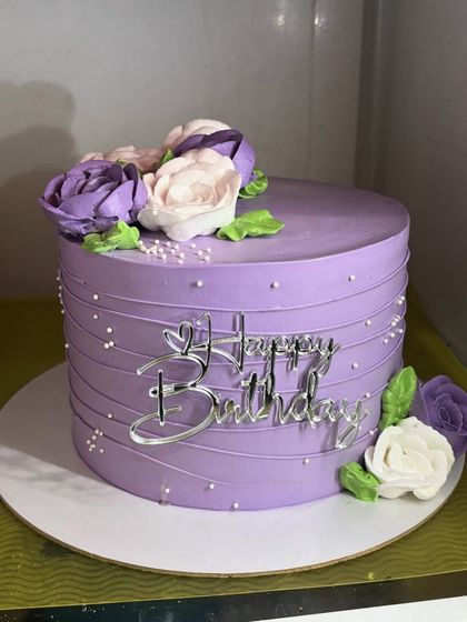 Simple, pretty, and classy, this purple whipped cream cake is adorned with hand-piped florals in shades of purple and white. The clean lines and delicate details make it a truly elegant choice.