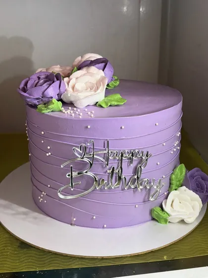 Simple, pretty, and classy, this purple whipped cream cake is adorned with hand-piped florals in shades of purple and white. The clean lines and delicate details make it a truly elegant choice.