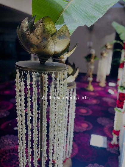 A close-up of a traditional brass lotus stand decorated with jasmine garlands. These small details add an authentic and sacred touch to any naming ceremony or pooja.