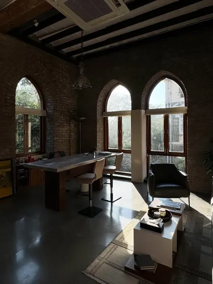 A quiet moment in the studio's lounge area. The afternoon sun streams through the large arched windows, highlighting the texture of the brick walls and the simple, comfortable furniture.