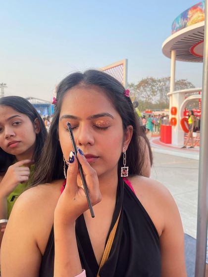 A close-up of an artist applying a gold glitter eyeshadow look at an outdoor festival.
