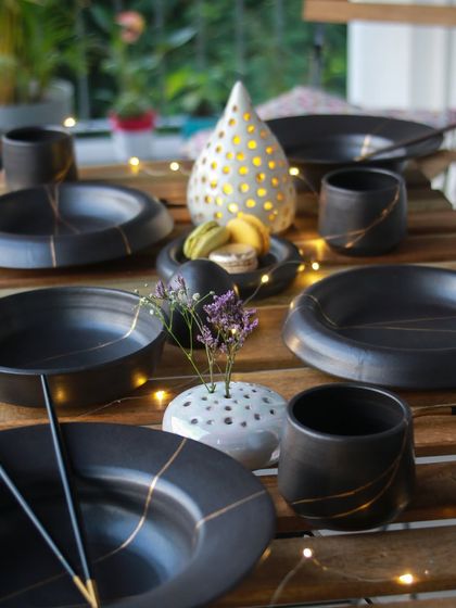 A full tablescape featuring the 'Celebrations' collection, with black dinnerware, luminaries, and flower frogs creating an elegant and memorable dining experience.