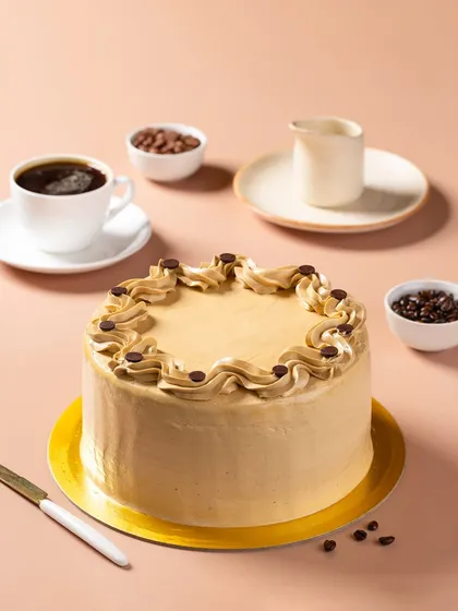 A coffee-flavored cake, styled with a cup of black coffee and coffee beans to communicate its flavor profile visually.