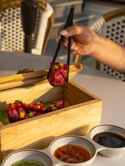 A hand using chopsticks to pick up a vibrant red dumpling. This lifestyle shot, set in a bright, sunlit cafe, feels natural and captures the experience of enjoying a meal.