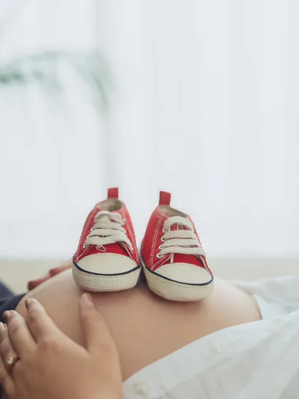 A creative and symbolic close-up of tiny red sneakers resting on the baby bump, announcing the little one's arrival in a fun, modern way.