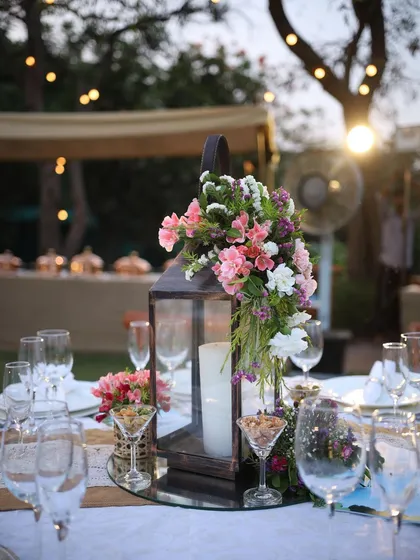 A rustic lantern centerpiece for an outdoor lunch. The lantern is decorated with a cascade of pink and white flowers, adding a touch of charm to the tablescape.