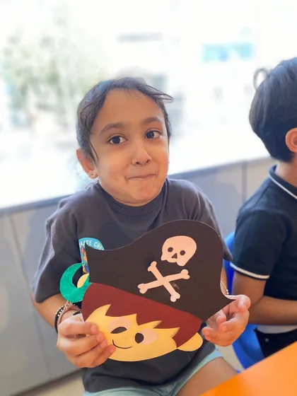 A girl gives a charming, expressive smile as she shows off the pirate mask she made.