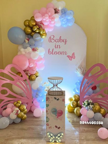 A beautiful "Baby in Bloom" baby shower with a butterfly theme. The pastel pink, blue, and gold balloon garland and large butterfly wing props create a magical and delicate setting.