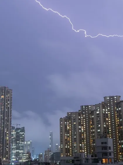 A horizontal lightning bolt flashes across the sky above a cluster of buildings in Mumbai.