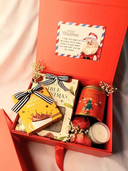 Spread the joy this season with a Christmas hamper. This festive red box is filled with hot chocolate mix, cookies, a scented candle, and other holiday treats.