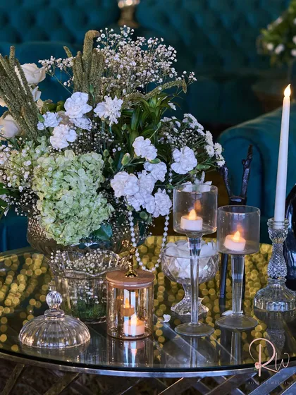 A tablescape detail, with a floral centerpiece, candles in modern glass holders, and a string of pearls, all reflecting in a mirrored table.
