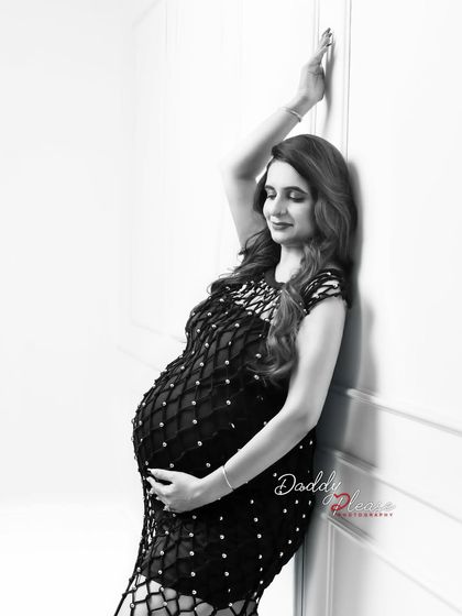 An elegant black and white portrait of a mother-to-be in a beautiful beaded dress. The high-contrast lighting and classic pose create a sophisticated and timeless image.